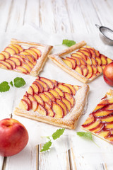 Refreshing delicious dessert, juicy nectarine puff pastry tarts with cream cheese and sprinkled with powdered sugar