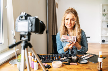 A young blonde woman talks about cosmetics and making a video for her beauty blog. Woman is holding a makeup palette and showing it at camera