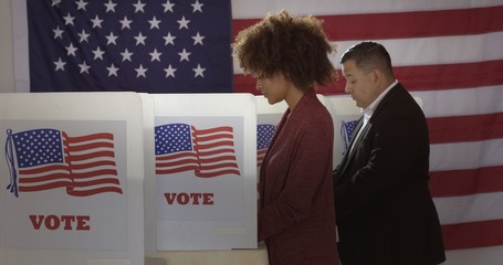 Profile, medium shot, young mixed-race woman and Hispanic man in polling station, voting in a booth...