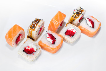 Japanese roll of rice, cream cheese, tobik, salmon, eel, sesame seeds, unagi sauce on a white plate