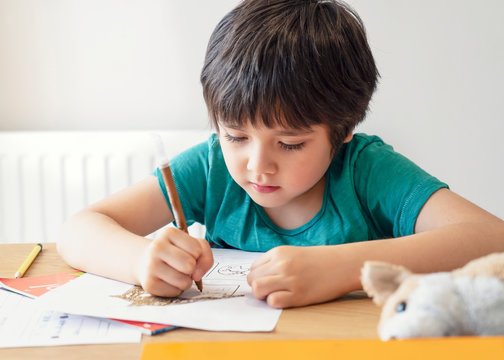 Portrait of school kid boy siting on table doing homework, Happy Child holding pencil writing, A boy drawing on white paper at the table,Elementary school and homeschooling concept