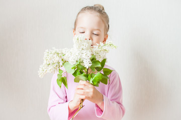 Little cute girl holding a bouquet of white lilac in her hands. Admires, looks, gives to mother. Mothers Day