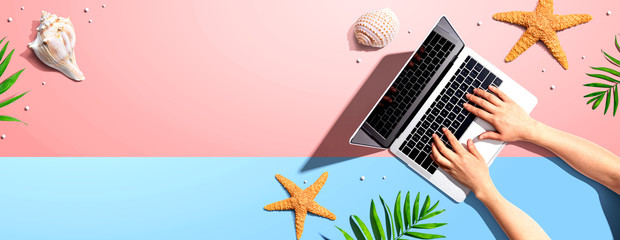 Person using a laptop computer with summer theme objects - flat lay