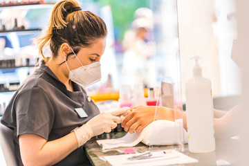 Fototapeta na wymiar A young Latina worker at a manicure and pedicure salon with security measures and face masks. The reopening due to the covid-19 pandemic. Coronavirus