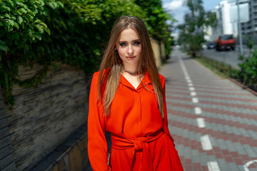 Photo of attractive woman wearing red dress on a green tree blurred background. Long hair. Portrait of a beautiful girl. Young female photo session.