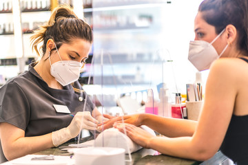 Obraz premium Manicure and pedicure salon with security measures and people with masks, performing a pedicure treatment. Reopening after the corod-19 pandemic. Coronavirus