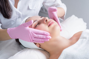 close-up, portrait of a young beautiful girl, with flawless skin, which the master masseur makes facial massage, in medical gloves. In a beauty salon