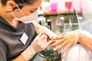 A worker with security measures and a face mask painting colored nails of the client. Reopening after the corod-19 pandemic. Manicure and Pedicure Salon. Coronavirus