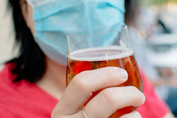 New normality. Woman drinking a beer with protective face mask on.