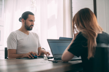 A man and a woman are working at a table at home