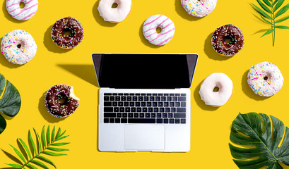 Laptop with donuts and tropical plants - flat lay