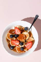 Pancake cereal with berries and honey on pink background