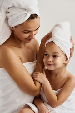 A young mother and her little daughter in white towels in the bedroom in the morning. Happy family at home.