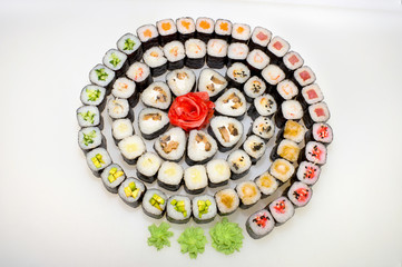 Maki set in the form of a spiral from traditional rolls of nori, rice, eel, shrimp, cucumber, avocado, ginger, sesame, cucumber, crab meat and wasabi on a white background