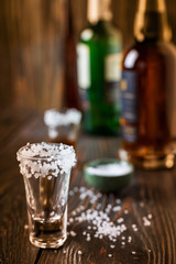 An empty tequila glass, with salt at the edges, stands on the bar, in the background are different bottles of alcohol, shallow depth of field, selective focus. The concept of a drink in the bar.