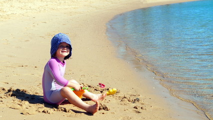 Joyful happy two year old baby girl playing with sand toys on the beach