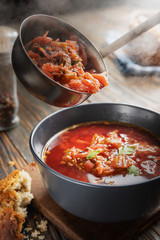 Tomato soup with vegetables and meat is poured into a bowl from the ladle from which steam comes, tasty, appetizing traditional Ukrainian borsch, close-up, shallow depth of field, selective focus