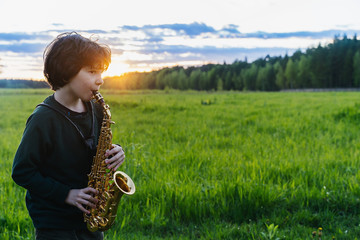 Boy plays saxophone in the sunset. Silhouette of a curly haired guy with a soprano saxophone 