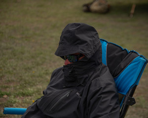 A man on a windy day with a rain jacket and sunglasses on.