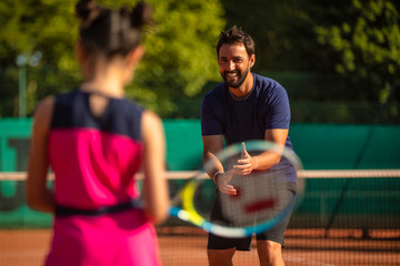 little girl from behind learning to play tennis with a tennis teacher