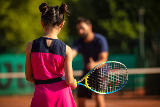 little girl from behind learning to play tennis with a tennis teacher