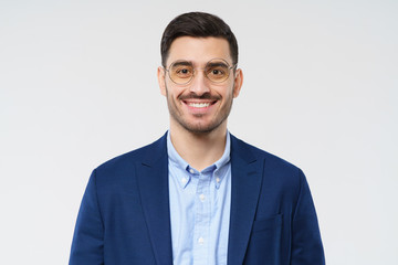 Close-up of businessman looking at camera with positive smile, wearing jacket, shirt and glasses, ready to help and support, isolated on gray background