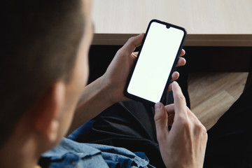 A businessman holds a mobile phone in his left hand and looks at the white screen of the mockup. Concept of online communication, work and technology