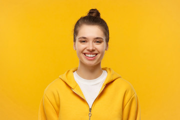 Portrait of young smiling teenage girl wearing white t-shirt and bright hoodie, smiling and feeling relaxed in free time, isolated on yellow background