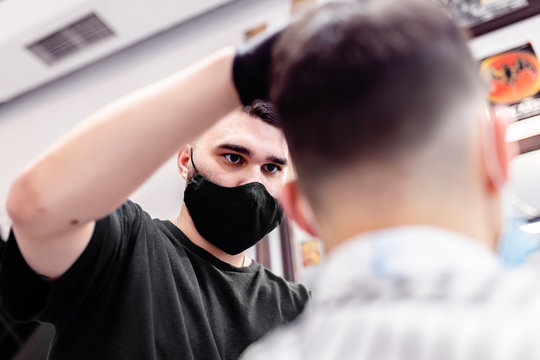 Men's haircut in a barbershop. Client and barber in anti-virus masks. 