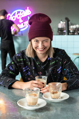 vertical frame young hipster girl sitting at table in front of several ended cups of coffee, with...