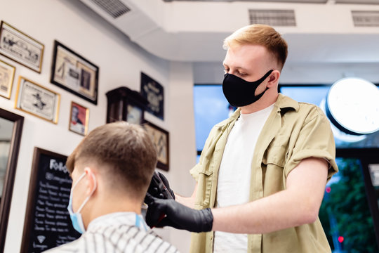 Men's haircut in a barbershop. Client and barber in anti-virus masks. 
