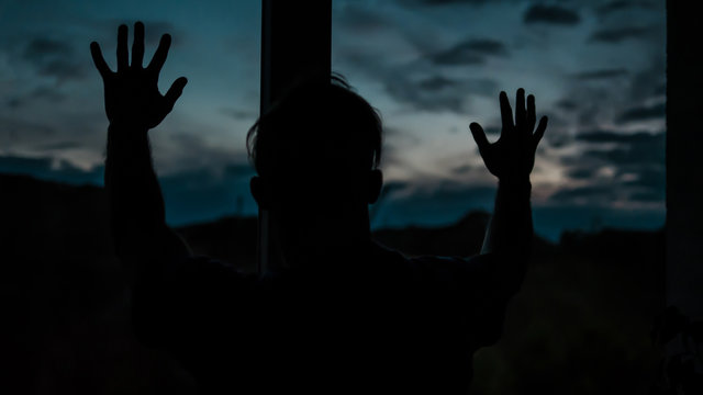 A Guy Looking Out The Window At Sunset.Sad And Upset Guy In The Apartment.Lifestyle Image Of A Young Man.