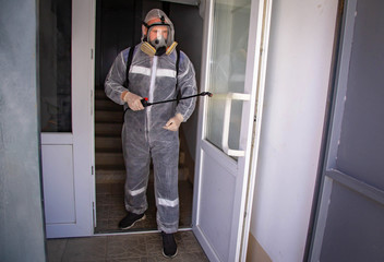 A man in a disposable suit for disinfection, his face is covered with a reusable mask with filters, and his hands are wearing latex medical gloves. Disinfects public premises, entrances, elevators fro