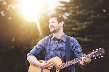 Young male in a park holding a guitar and playing a song from the Christian hymn book