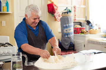 Hispanic adult man preparing bread dough - grandfather cooking at home - man with gray hair making artisan bread