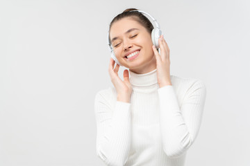 Young female relaxing to sounds of music she is listening in wireless headphones with smile, isolated on gray background