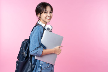 Fototapeta Portrait of smiling young Asian college student with laptop and backpack isolated over pink background obraz