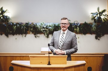 Male in a formal outfit preaching the Holy Bible from the tribune at the altar of the church