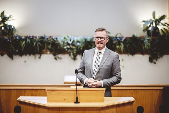Male in a formal outfit preaching the Holy Bible from the tribune at the altar of the church