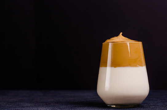 Dalgon coffee in a glass loom made of instant coffee, sugar, hot water and milk, a new trendy cold drink on a dark background.