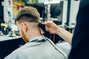 Male haircut with electric razor. Barber makes haircut for client at the barber shop by using hairclipper. Man hairdressing with electric shaver.