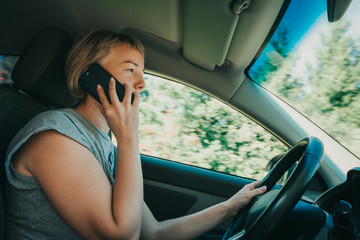 Fototapeta na wymiar Woman drives car holding smartphone in hand and talking. Concept of unsafe driving auto at high speed. Girl violated law, danger of accident. Busy driver distracted from road, risk and careless