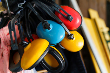 Red yellow and blue ear muffs hanging in storage basement or room in day close up ear sound noise...