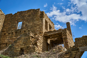 An abandoned stone house on a Sunny day. An old building, an empty city on a mountain, and a blue sky. Broken stone walls.