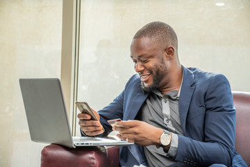 a young african businessman using his credit card and mobile phone, online banking concept