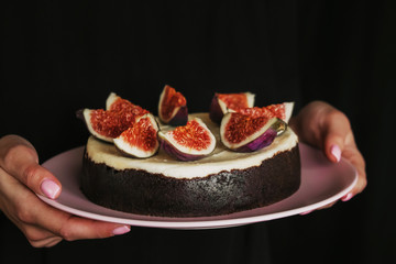 woman holding a pink plate with a cheesecake. a chocolate dessert with fresh figs isolated on a dark black background. minimalism cake design. a female hand with baby pink nails fresh manicure