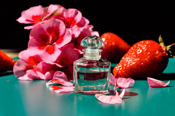 Beautiful contrast composition with elegant small perfume bottle, pink flower and strawberries on the dark background. Selective focus.