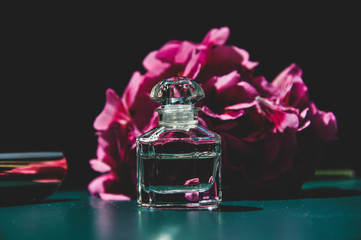 Beautiful vintage composition with elegant small perfume bottle and pink flower on the dark background. Vintage style photo. Selective focus.