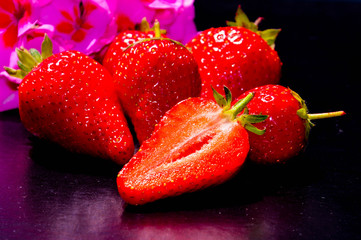 Beautiful ripe red strawberries on the black background against the blurred purple flower. Close up cut berries.