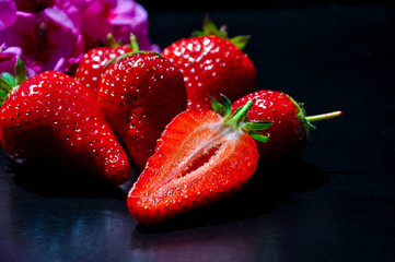 Beautiful ripe red strawberries on the black background against the blurred purple flower. Close up cut berries.